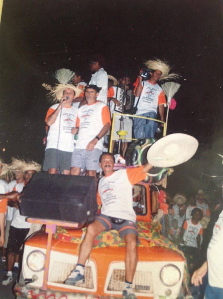 Foto da primeira edição do Arrasta-Pé Zona Rural: foliões em cima de uma rural laranja com sanfona e chapéus de palha, à noite
